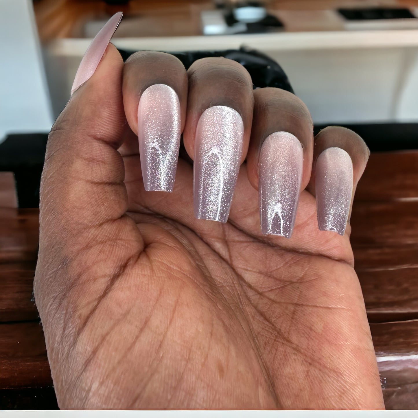 Hand featuring long coffin-shaped nails with silver ombre color against a brown background
