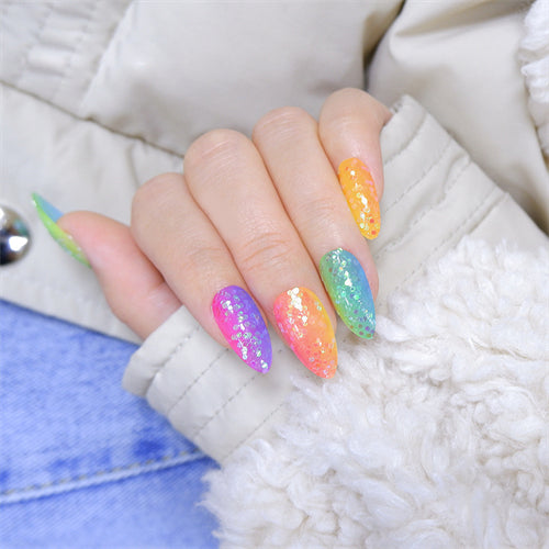 A hand adorned with almond-shaped press-on nails in a vibrant rainbow of colors, resting on a white fabric