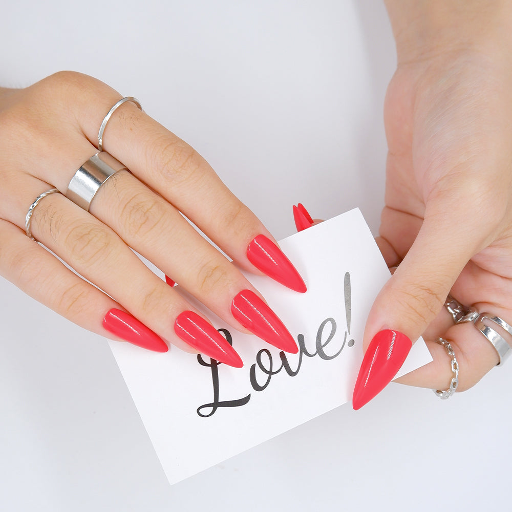 Hand showing fingers in Tart red long stiletto press-on nails holding a card with the word love written on it.